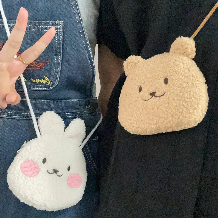 Two small plush bags, one white with pink cheeks and the other beige with a Kawaii bear design, held by people.