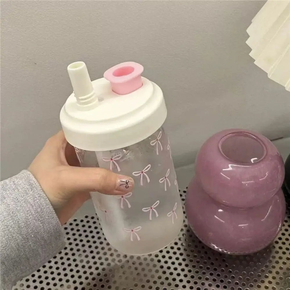 Clear tumbler with Kawaii pink bows and a pink lid held by a hand, next to a purple container on a perforated metal surface.