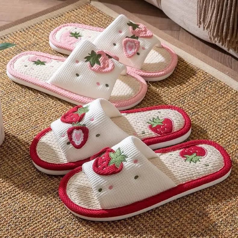Pair of white slippers with red strawberry kawaii designs on a woven mat.