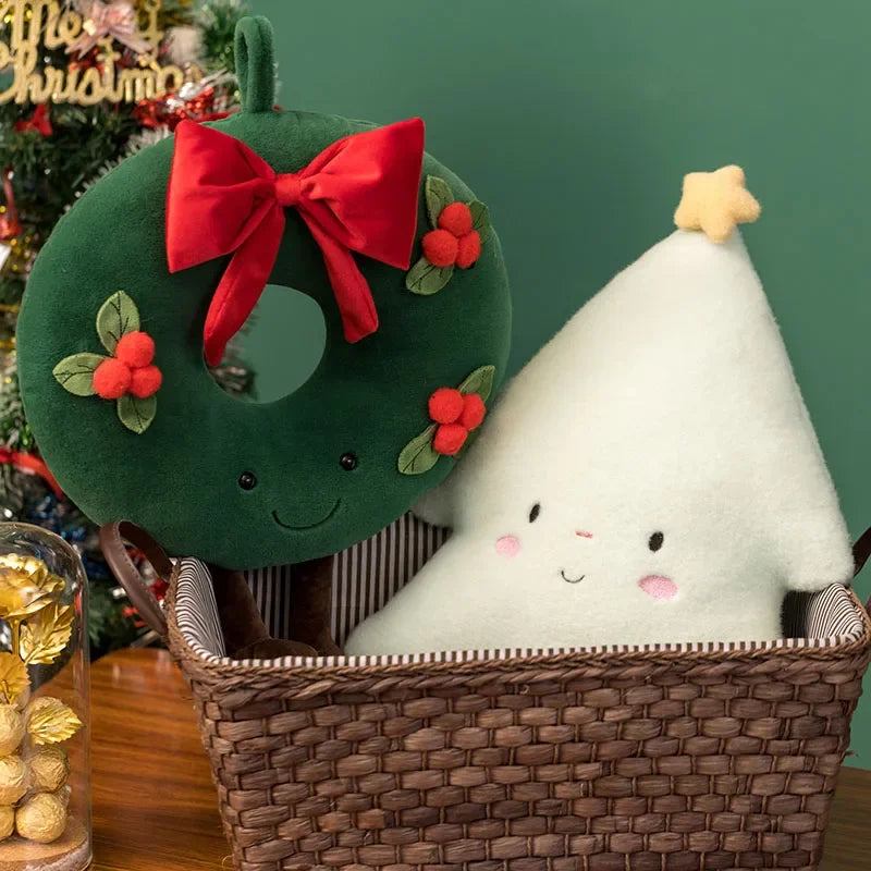 Green wreath plush toy with a red bow and white tree kawaii plush toy in a basket, Christmas decorations in the background.
