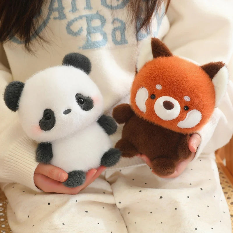Two plush kawaii toys, a panda and a red panda, held by a person wearing a light-colored sweater.