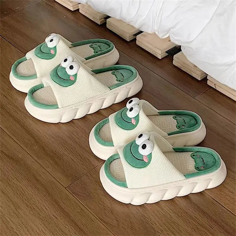 Pair of cartoonish kawaii slippers with green accents on a wooden floor.
