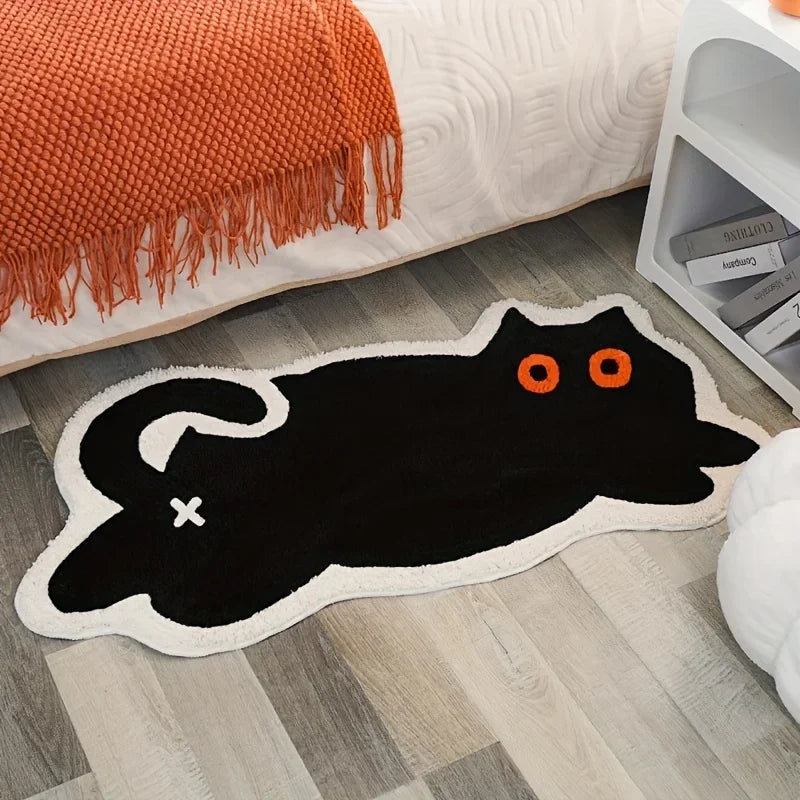 Black cat-shaped kawaii rug on a wooden floor with an orange blanket and white cabinet in the background.