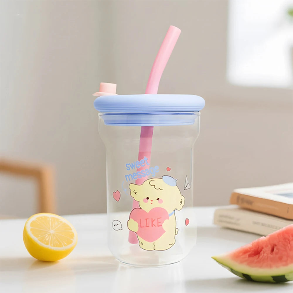 Clear tumbler with a Kawaii cartoon bear holding a heart-shaped 'LIKE' sign, pink straw, and blue lid on a table with a lemon and watermelon.