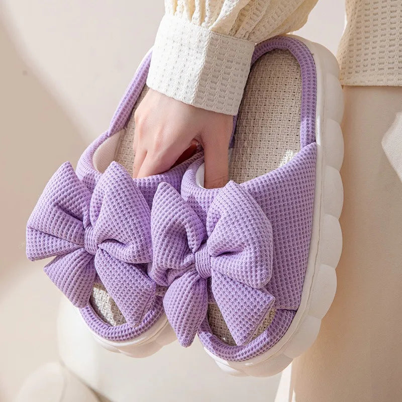 Purple kawaii slipper with a large bow held by a person wearing a white sweater.