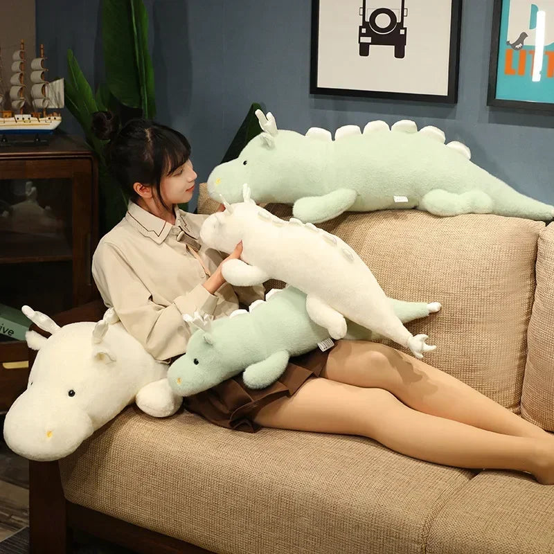 Woman sitting on a couch holding large kawaii plush dragons in a living room setting.