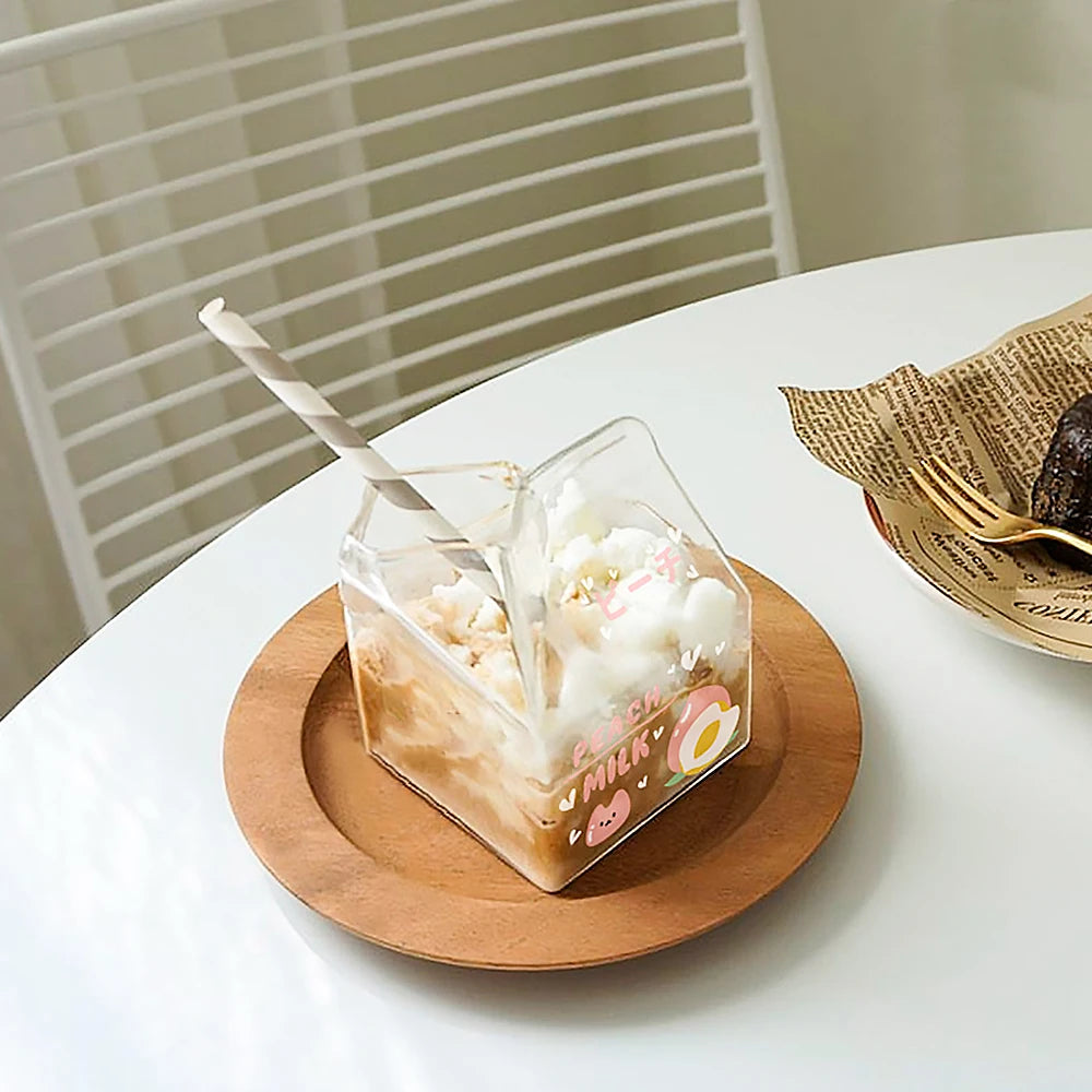 Square Kawaii-style glass with a straw on a wooden coaster on a white table