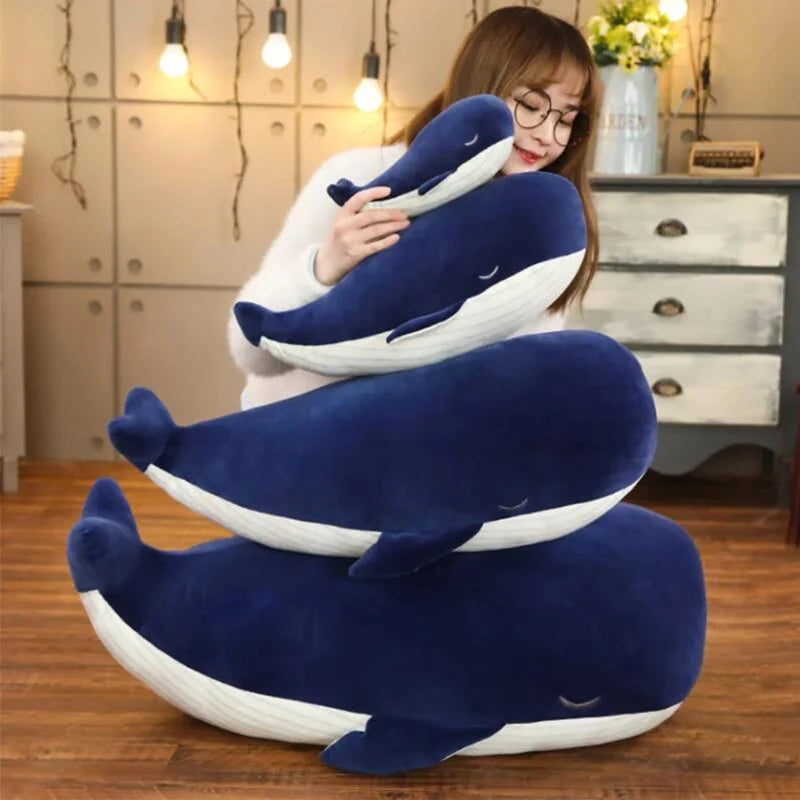 Person holding a stack of blue and white whale-shaped kawaii pillows in a room.