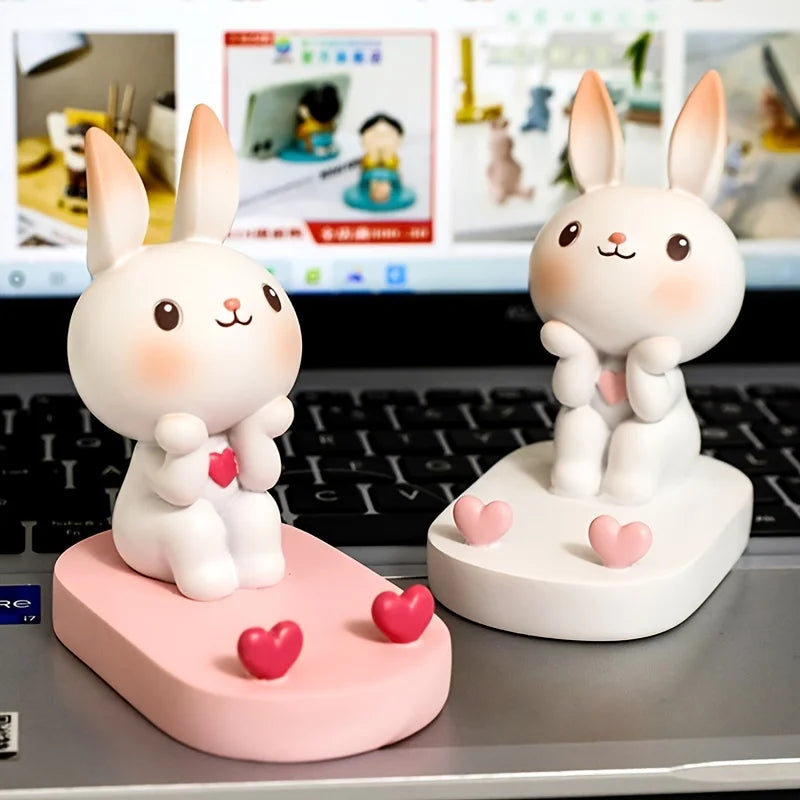 Two cute rabbit kawaii figurines with pink hearts on a desk in front of a computer screen.
