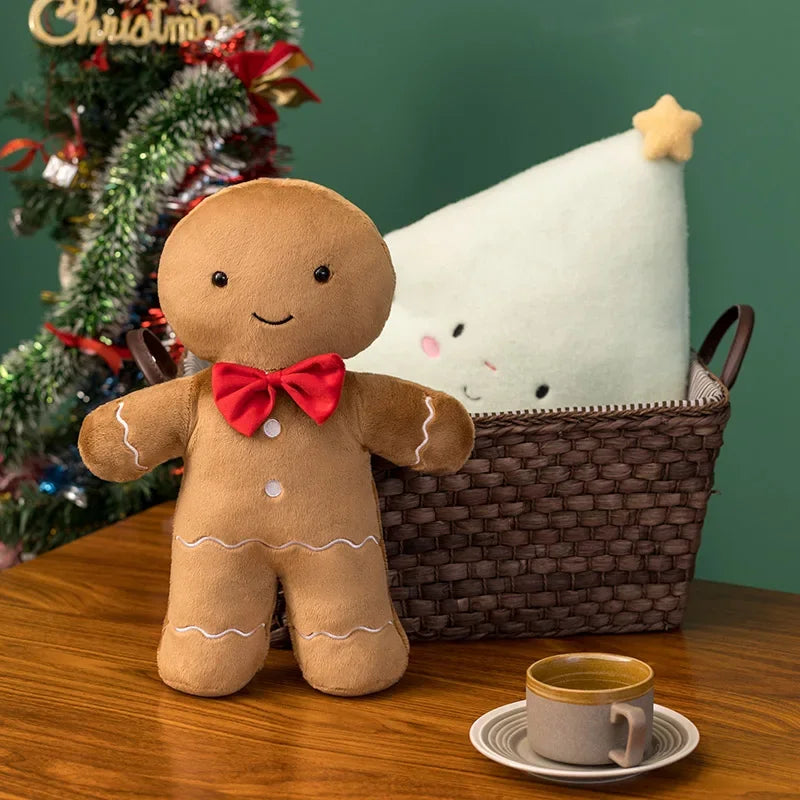 Gingerbread man kawaii plush toy with a red bow tie on a table with a Christmas tree in the background.