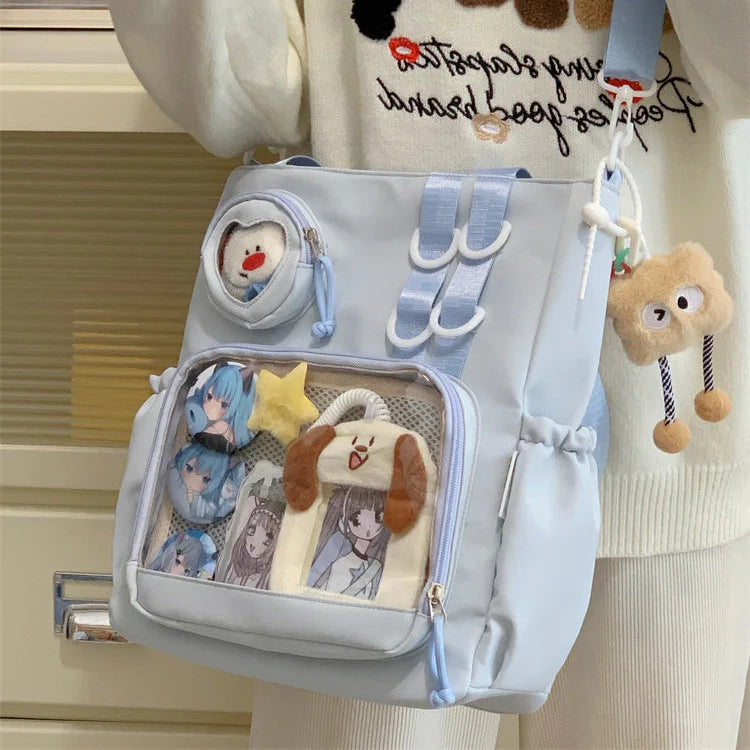 Light blue Kawaii backpack with cartoon character designs held by a person wearing a white sweater with embroidered characters.