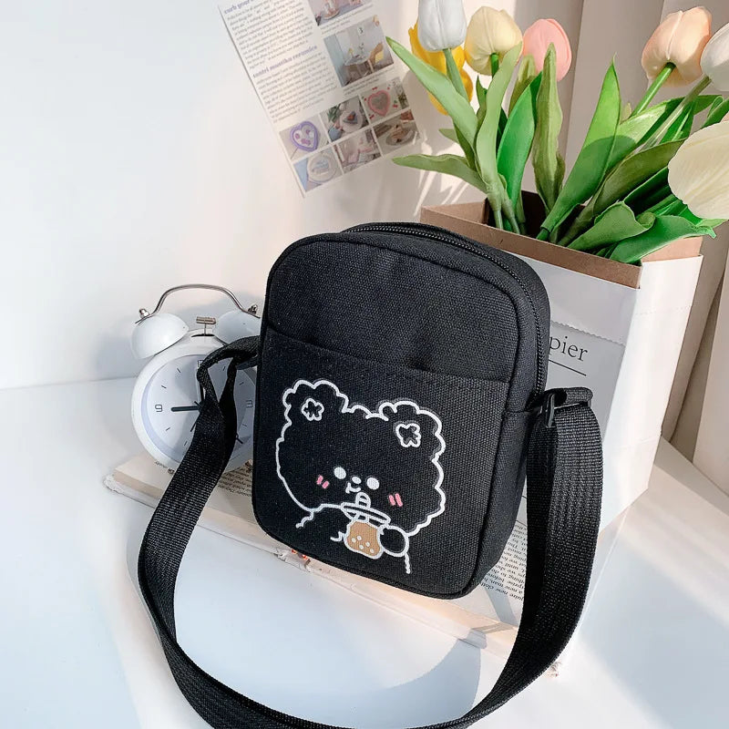 Black crossbody bag with a Kawaii cartoon design on a surface with flowers and an alarm clock in the background