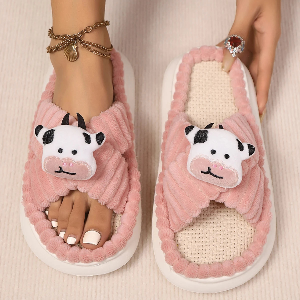 Pink slippers with kawaii cow face design worn by a person on a beige background
