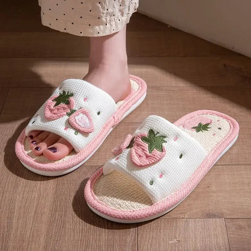 White slippers with kawaii pink strawberry designs on a wooden floor