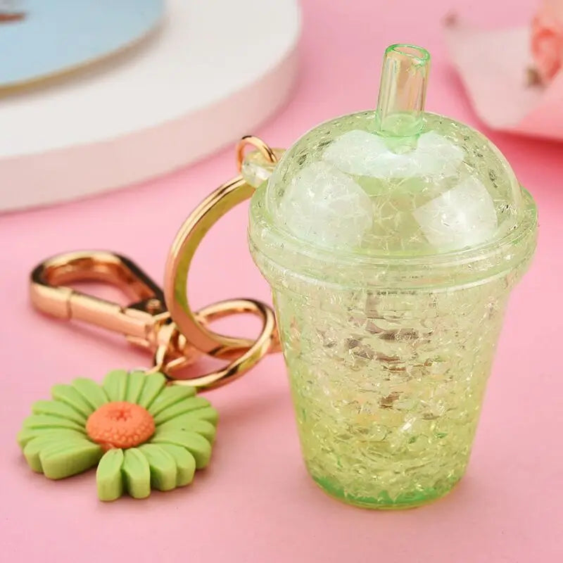 Keychain shaped like a kawaii green cup with a straw and flower charm on a pink background