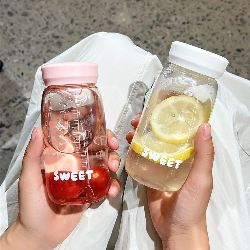 Two hands holding transparent Kawaii-style bottles with pink and white lids, filled with red and yellow liquids labeled 'SWEET'.