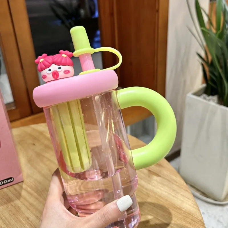 Clear Kawaii water bottle with pink and green handle and straw attachment held by a hand.