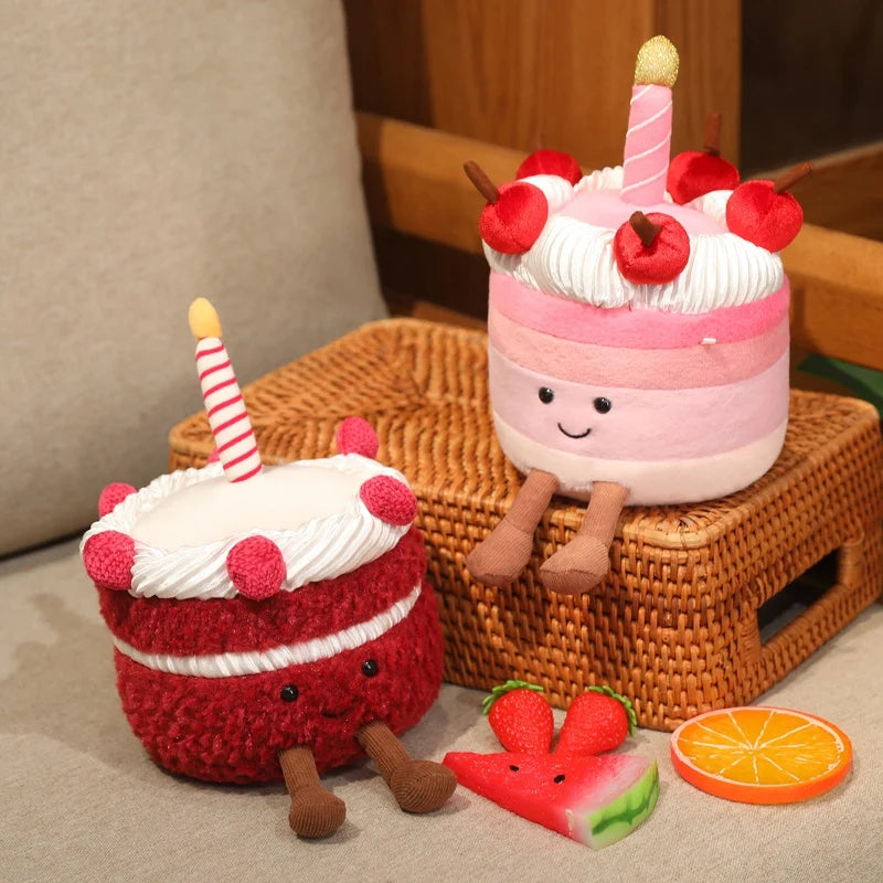 Two plush kawaii toys resembling birthday cakes with candles on a woven surface.