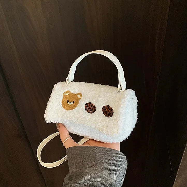 White fluffy handbag with a Kawaii teddy bear design held against a dark background