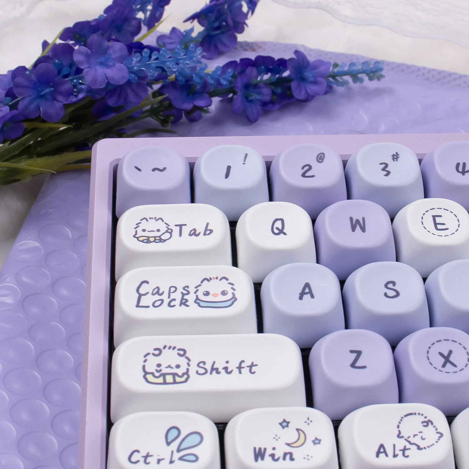 Keyboard with Kawaii character designs on keys, placed on a textured surface with purple flowers.