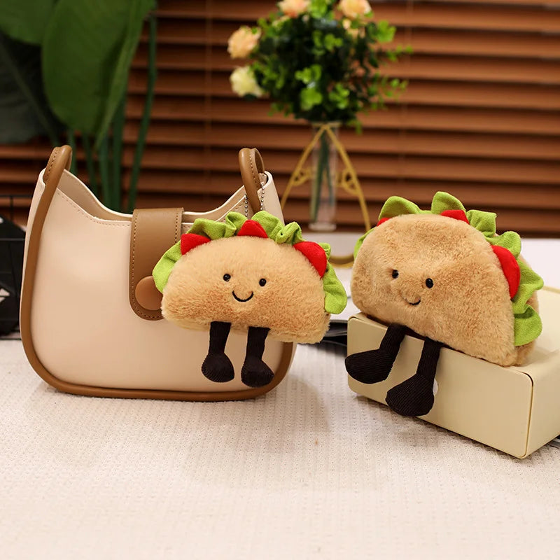 Two kawaii plush taco toys attached to a beige handbag on a light surface with a blurred background.