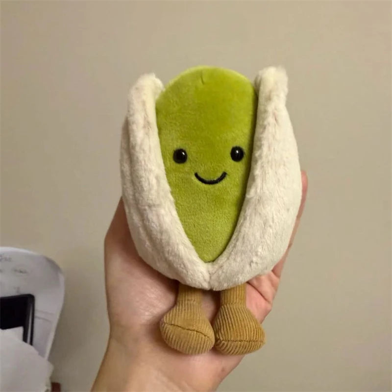 Plush kawaii toy resembling a pistachio with a smiling face held in a hand against a neutral background