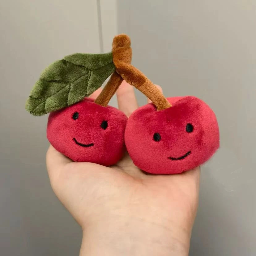 Plush toy kawaii cherries with smiling faces held in a hand against a neutral background