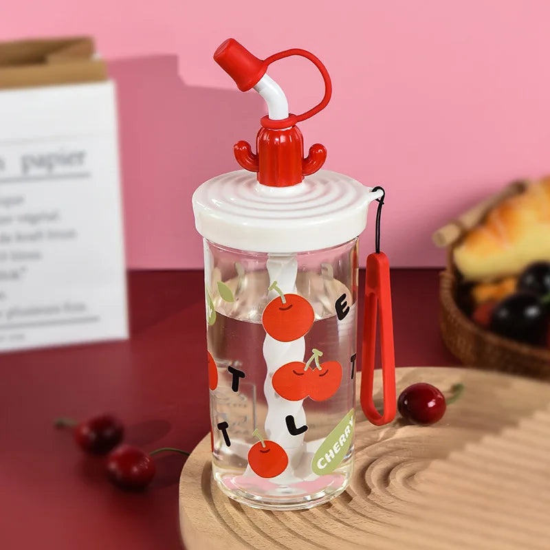 Clear water bottle with Kawaii cherry design and red straw lid on a wooden surface with pink background