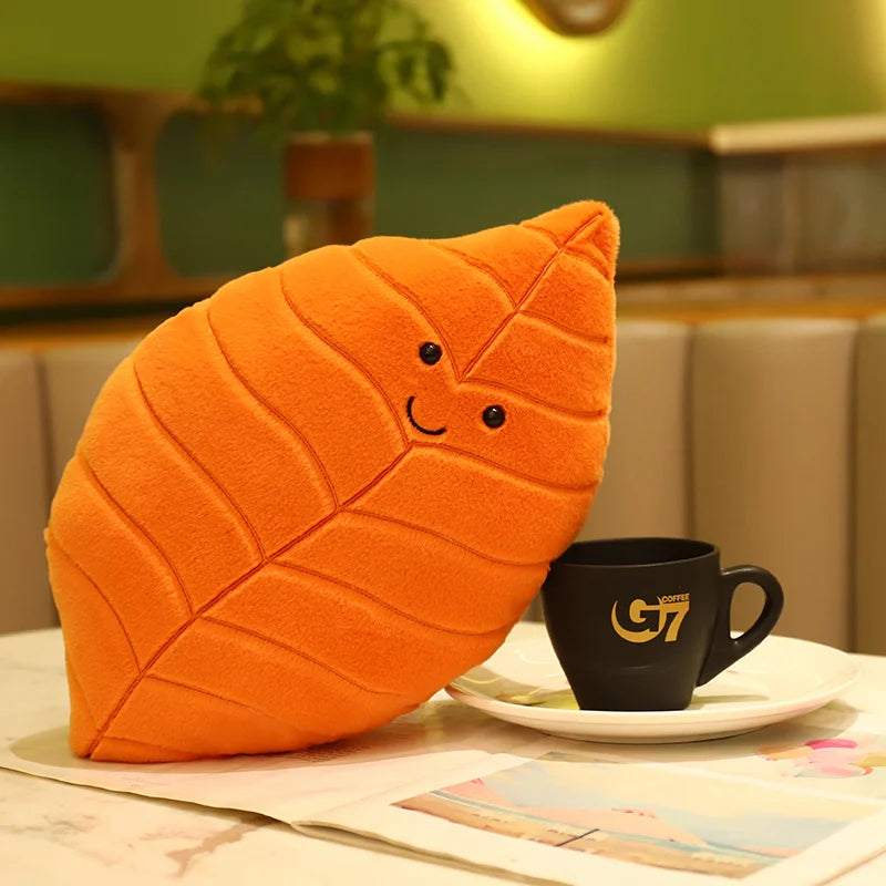 Plush kawaii toy shaped like a leaf with a smiley face next to a black G7 coffee cup on a table.