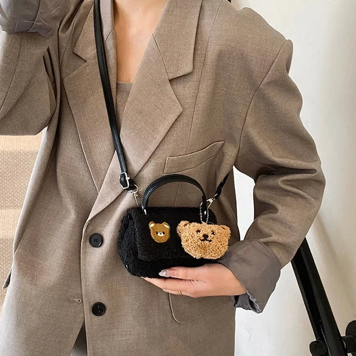 Person holding a black handbag with Kawaii teddy bear charms, wearing a beige suit.