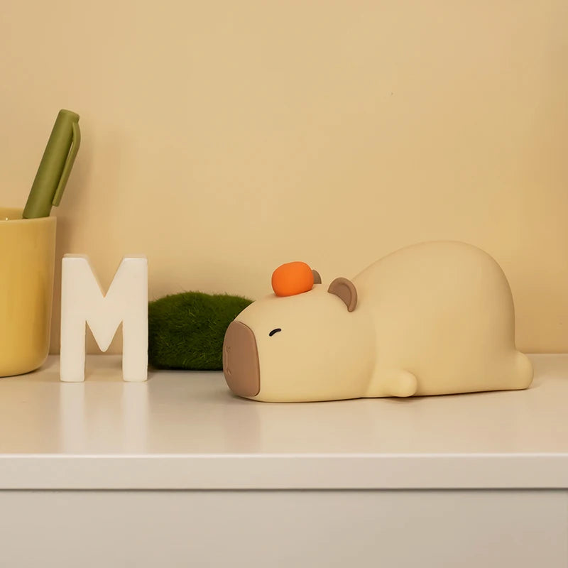 Small white kawaii animal figurine with an orange on its head next to a letter 'M' on a shelf.