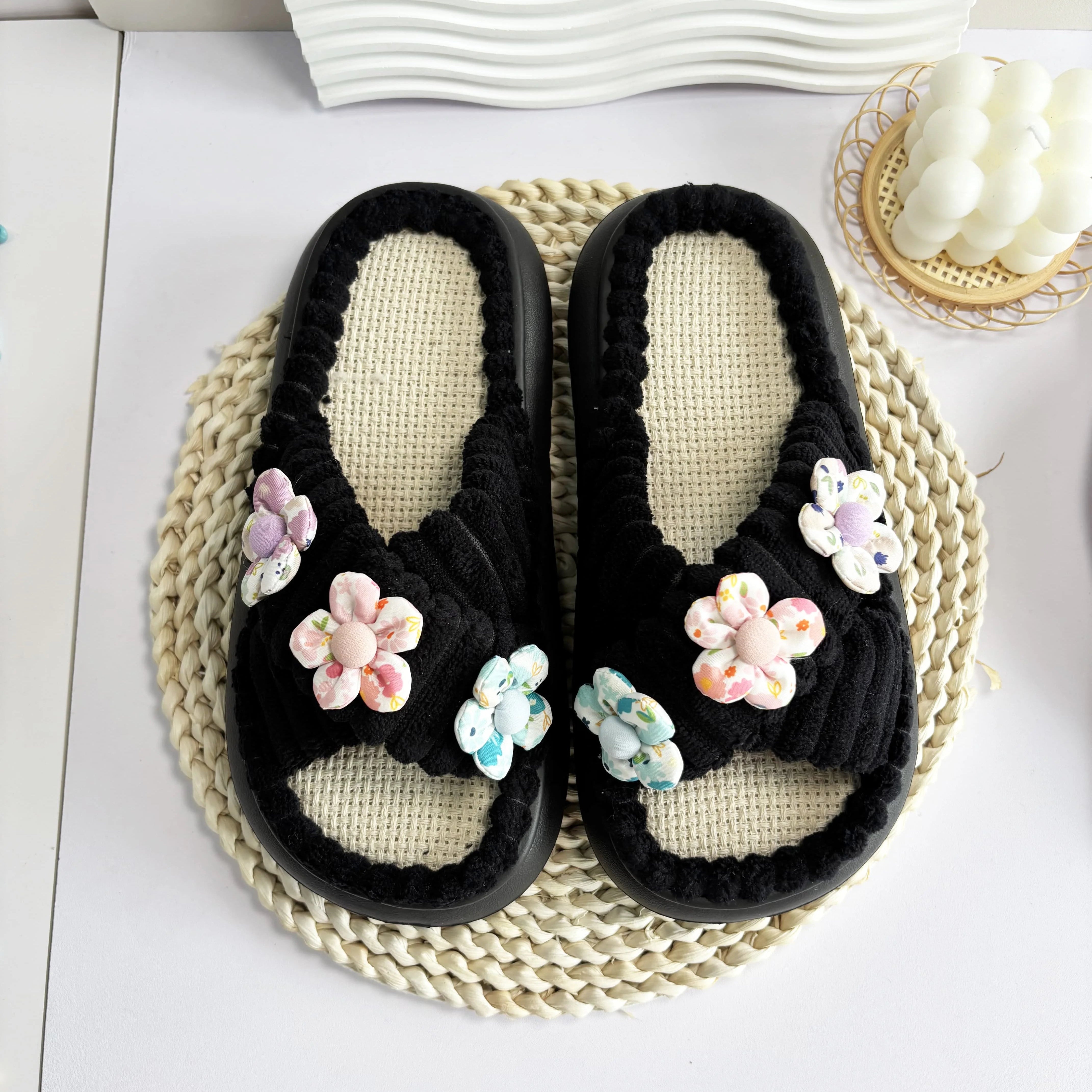Black slippers with kawaii floral decorations on a woven mat