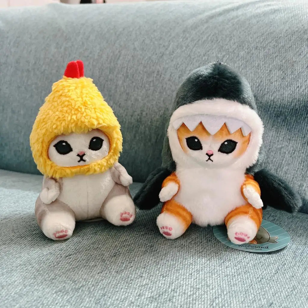Two kawaii plush toys, one resembling a chicken and the other a shark, sitting on a gray surface.