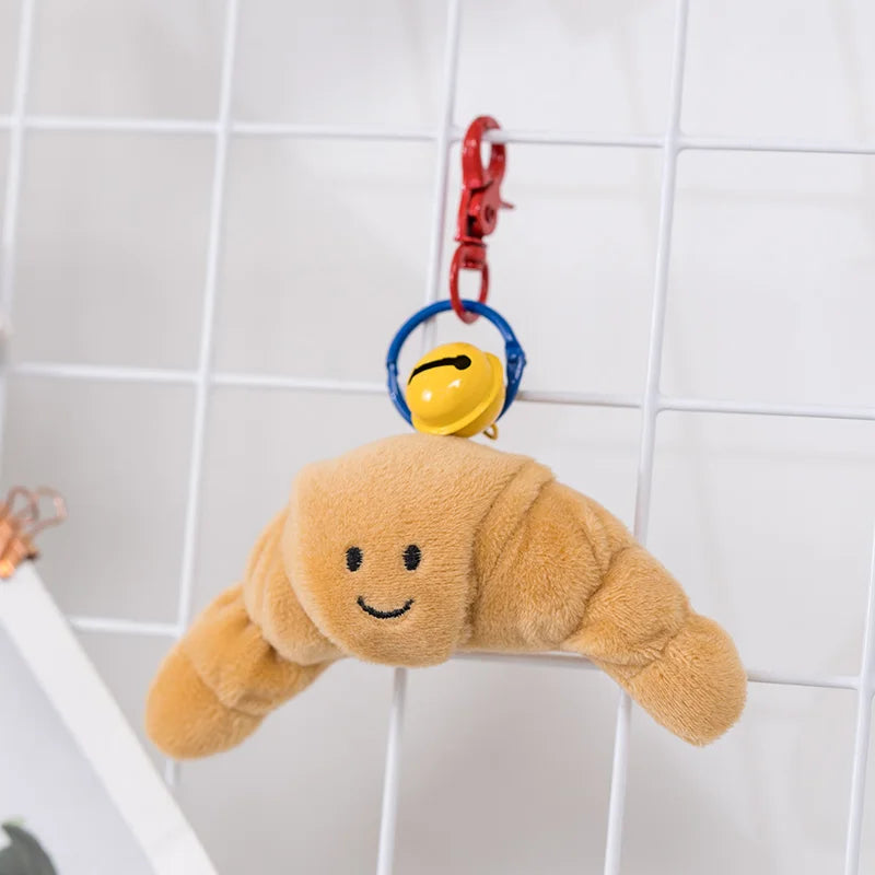 Plush croissant kawaii toy with a keychain on a tiled wall background