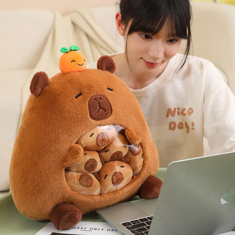 Person sitting on a couch with a large brown kawaii plush toy resembling a bear with smaller toys inside, using a laptop.