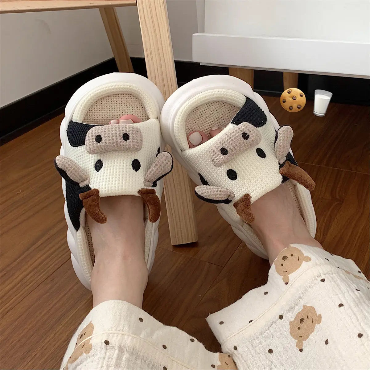 White slippers with kawaii cartoon cow design worn indoors on a wooden floor.