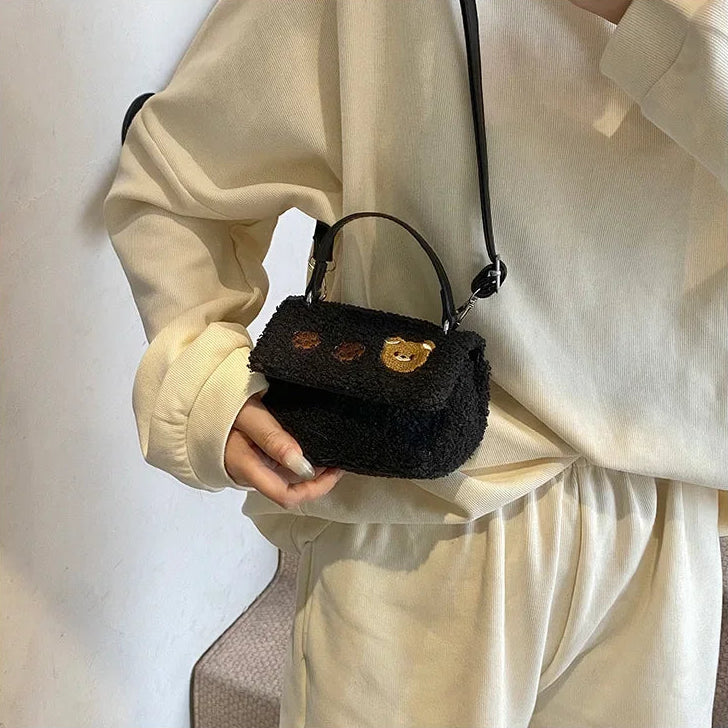 Person holding a small black textured handbag with Kawaii bear face design against a neutral background