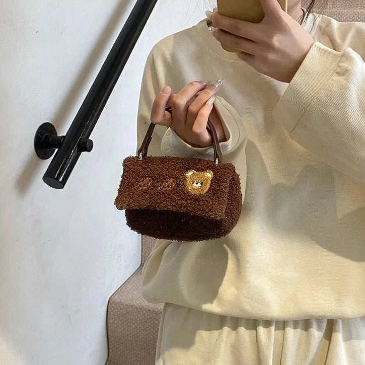 Person holding a Kawaii brown teddy bear-shaped handbag against a white wall.