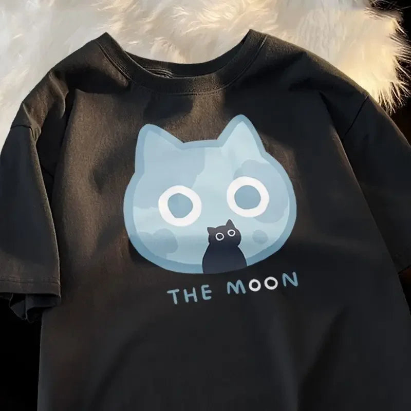 Black t-shirt with a kawaii graphic of a cat inside a moon and 'THE MOON' text, against a fluffy white background.