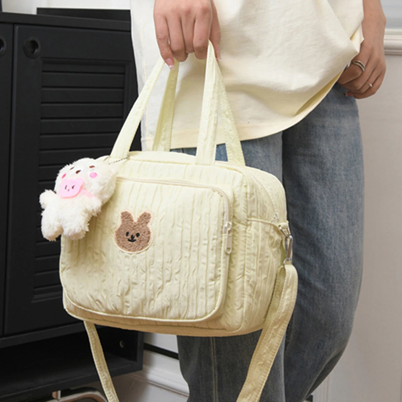 Beige textured handbag with a Kawaii bear emblem held by a person wearing a white shirt and jeans.