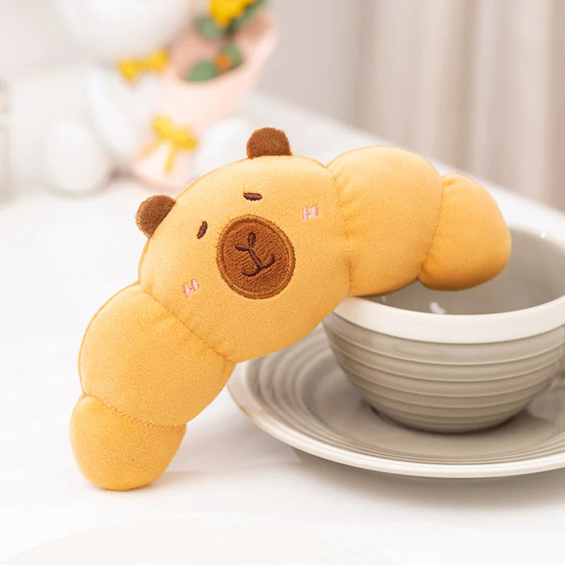 Plush kawaii toy shaped like a croissant with a face on a white surface with a blurred background