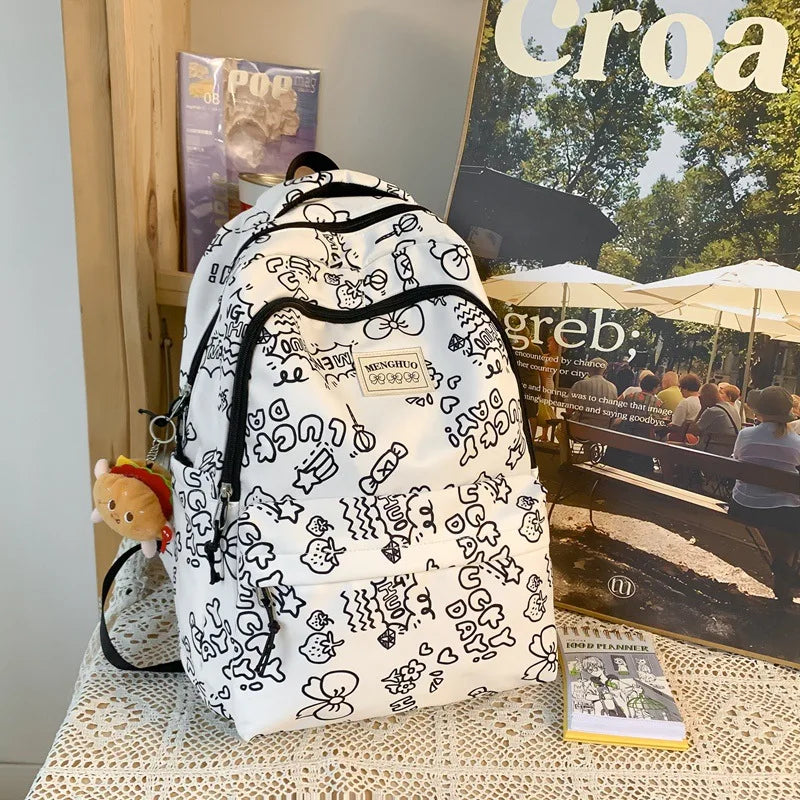 White backpack with black patterns on a table with magazines and a small Kawaii plush toy.