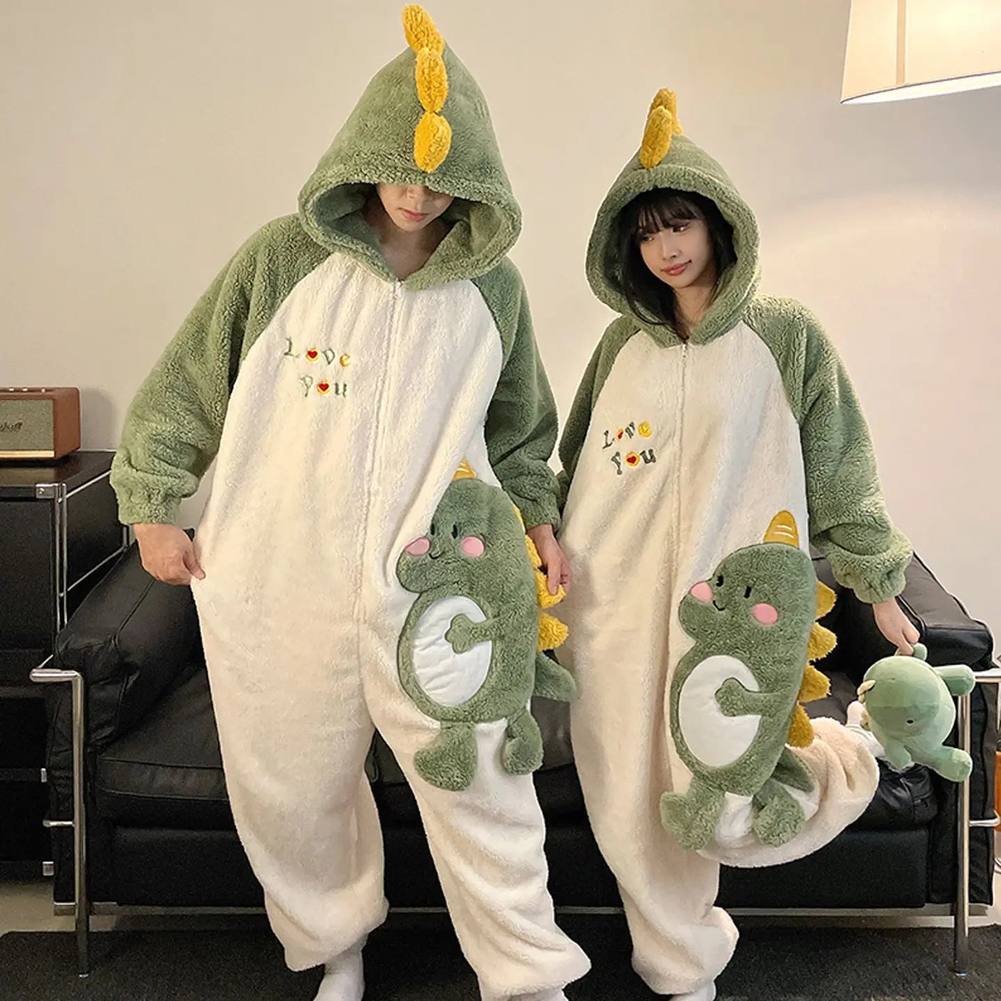 Two people wearing kawaii dinosaur-themed onesies in a living room setting.