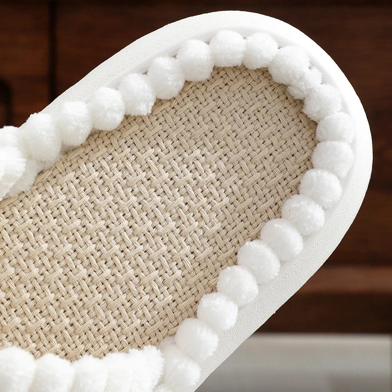 Close-up of a woven kawaii shoe with white pom-pom trim on a wooden floor.