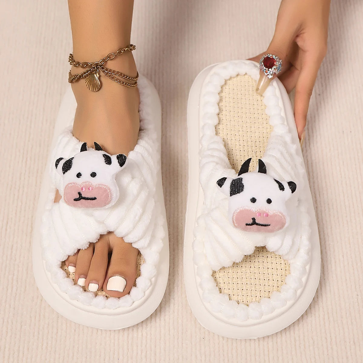 White slippers with cow face kawaii design worn by a person on a beige background
