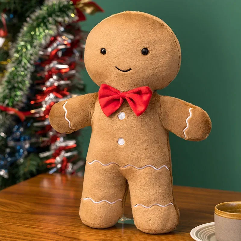 Kawaii plush gingerbread man toy with a red bow tie on a wooden table with a Christmas tree in the background.