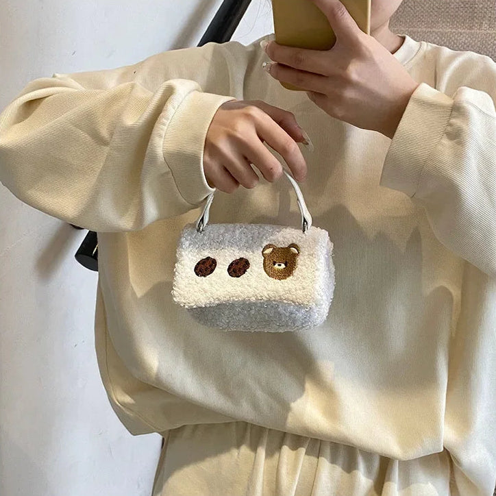 Person holding a small fluffy bag with Kawaii bear faces on a plain background