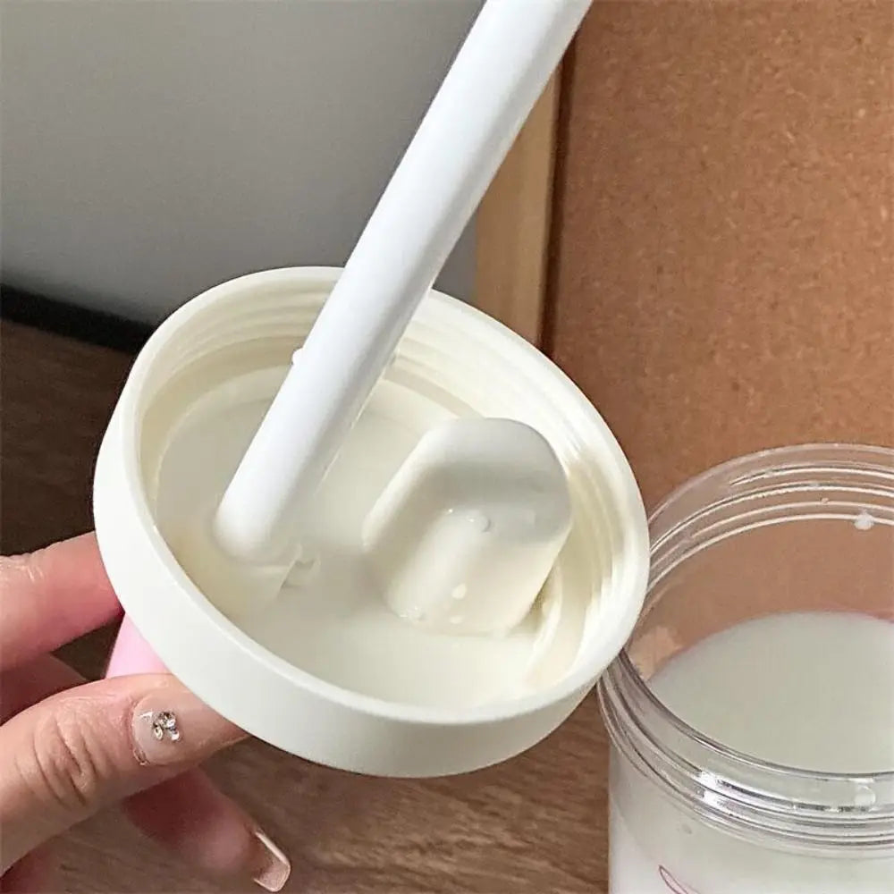 Hand holding a Kawaii-style container of white cream with a spoon, with a cardboard box in the background.
