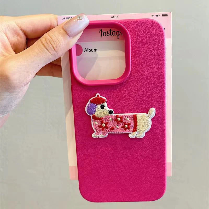 Pink phone case with embroidered kawaii dog design held by a hand
