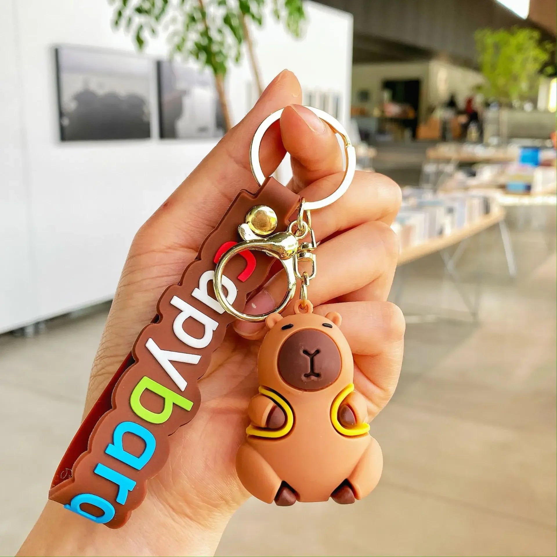 Hand holding a kawaii keychain with a bear design and colorful text in an indoor setting.